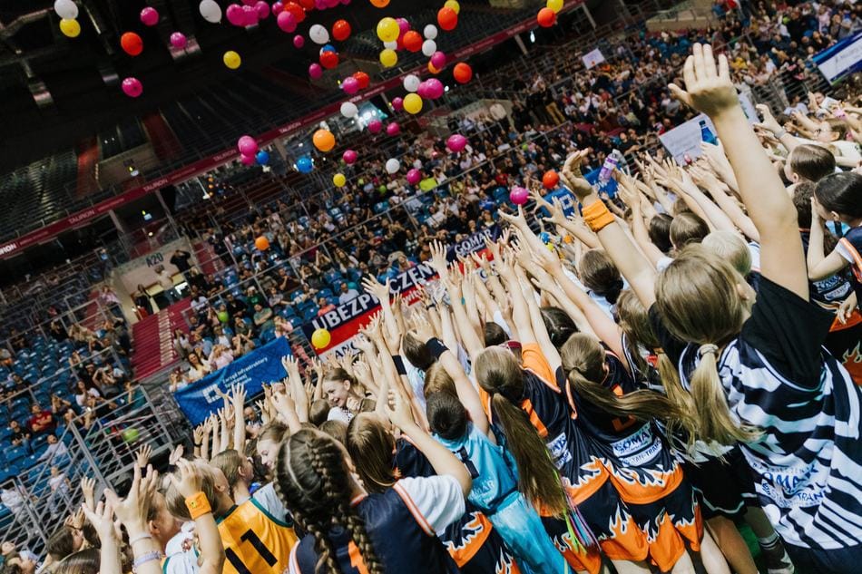 Rodzice na trybunach i dzieci z rękami w górze pod balonami