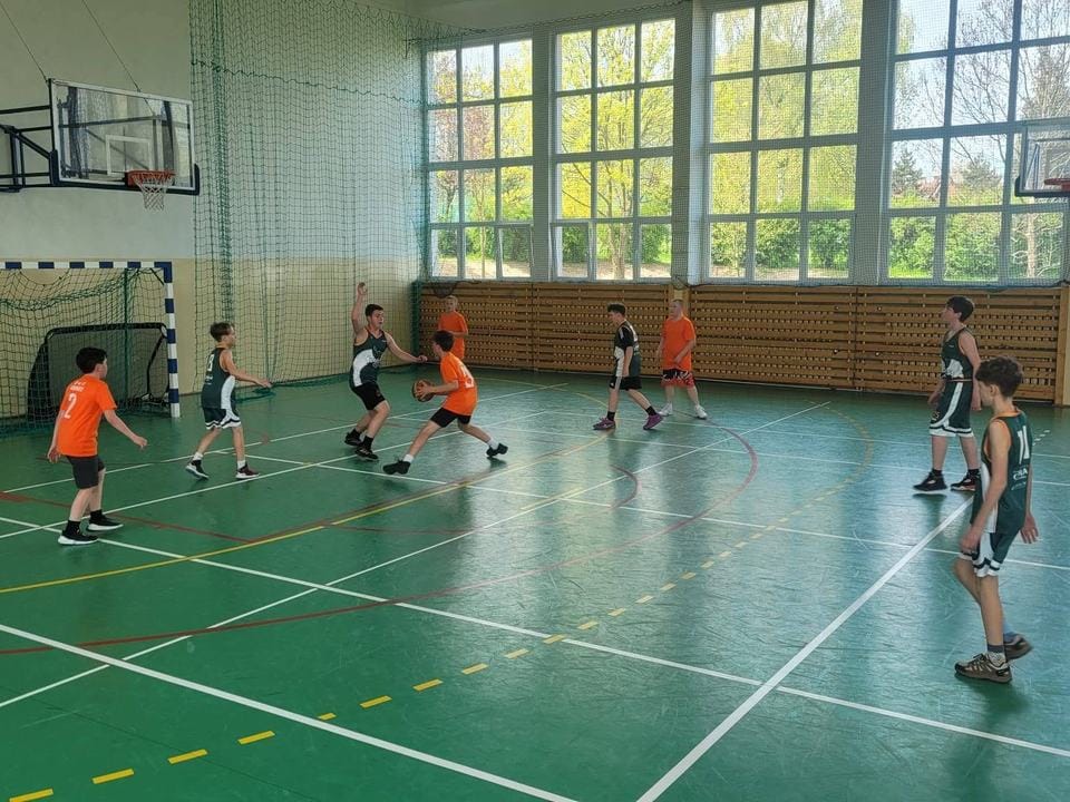 Mecz w gminnej hali sportowej, drużyny w zielonych i pomarańczowych strojach